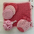 Handmade crochet bath set with pink, rose, and white cotton yarn poufs and face scrubbies arranged on neutral background